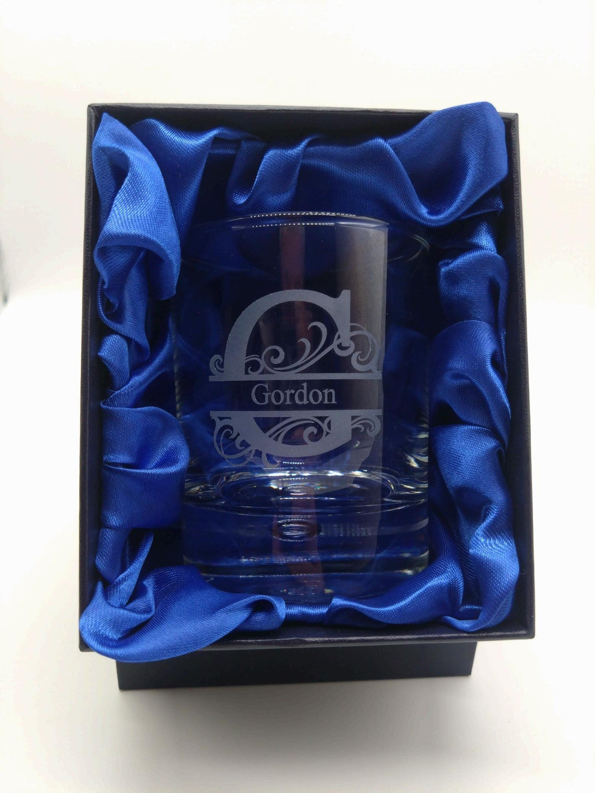 Glass tumbler with engraved design and 'Gordon' text, placed in a blue box with blue satin lining.