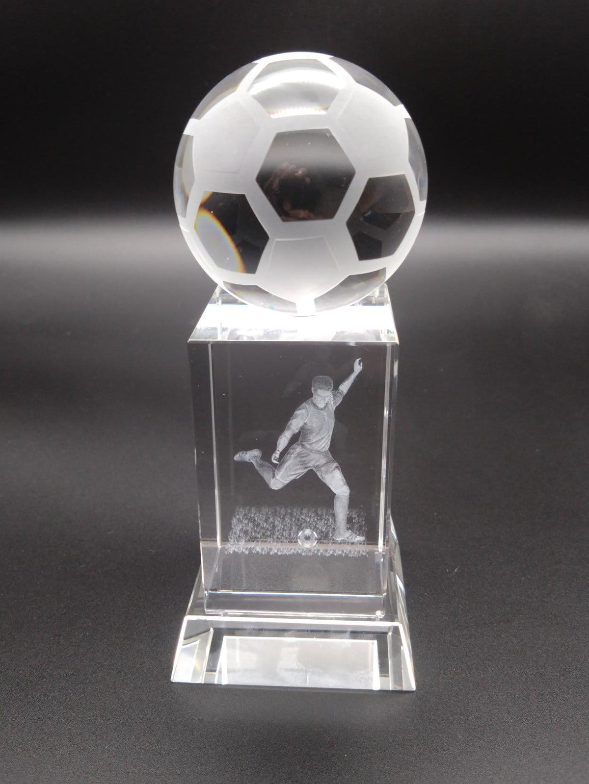 Crystal soccer ball trophy with a player on a dark background