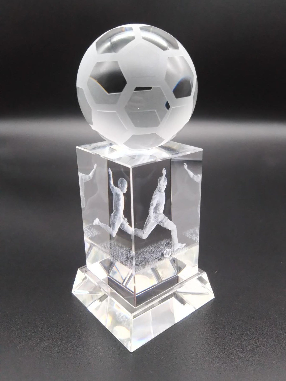 Crystal soccer ball trophy with player figures on a dark background