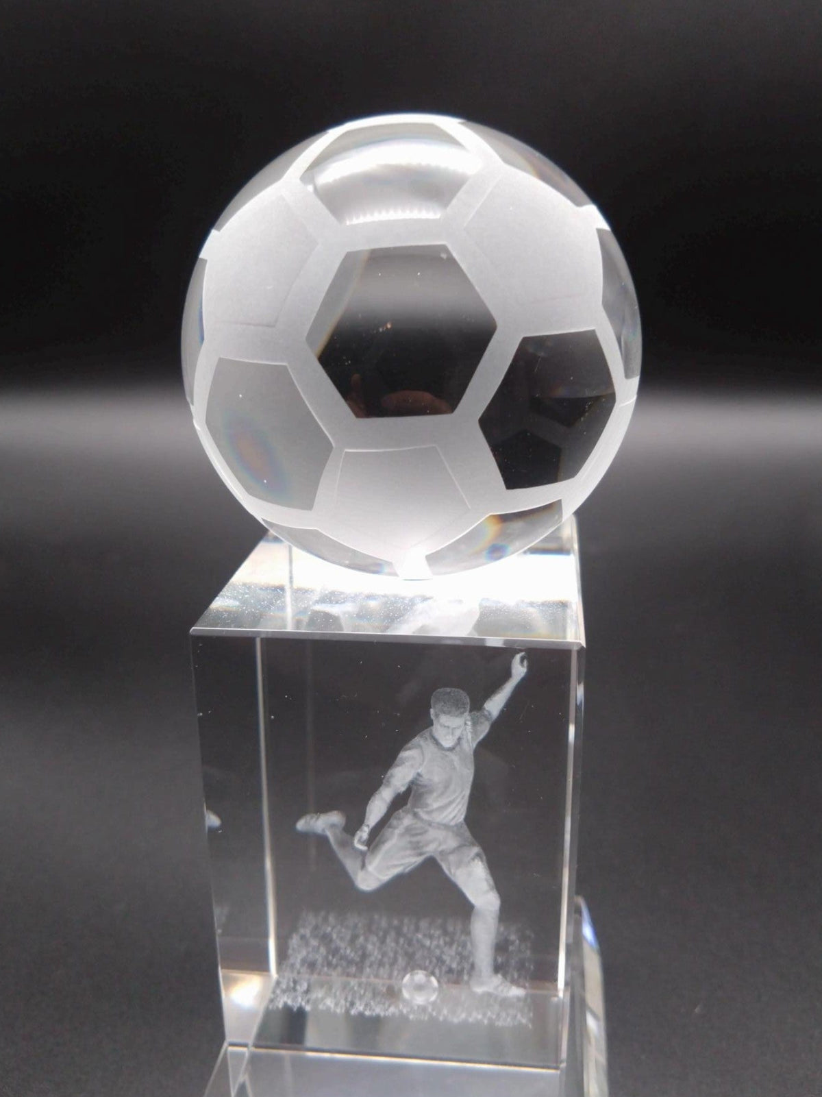 Crystal soccer ball on a pedestal with a engraved player image against a dark background