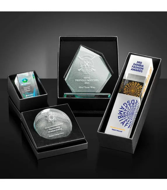 Collection of engraved glass awards in black boxes on a dark surface