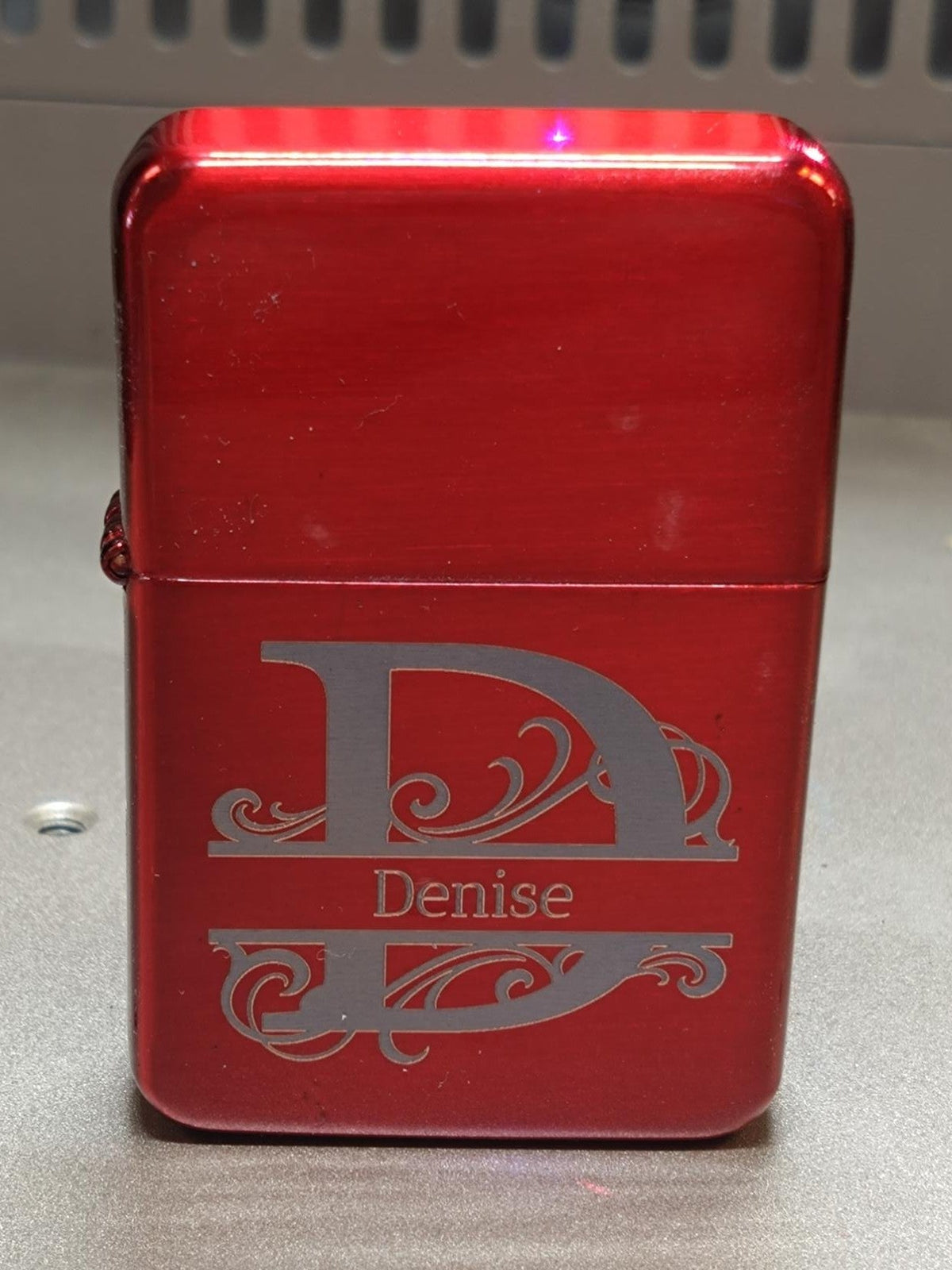 Red lighter with 'Denise' engraved on a metallic surface
