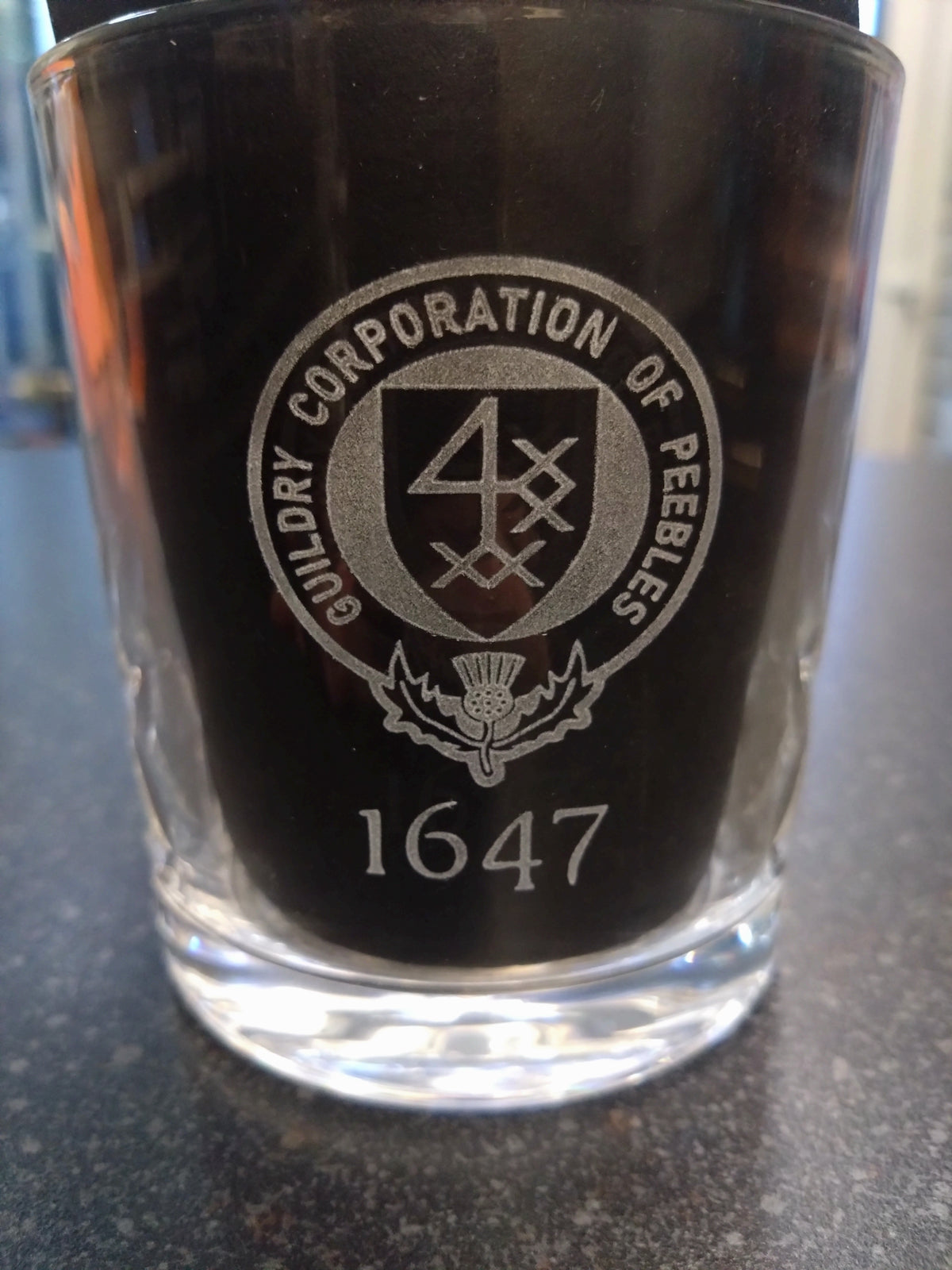 Whisky glass with engraved logo and text on a reflective surface