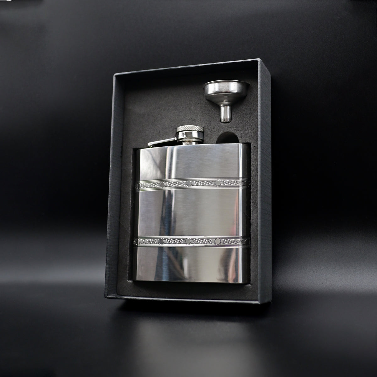 Silver hip flask with funnel in a black box on a dark background