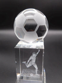 Crystal soccer ball on a pedestal with a engraved player image against a dark background