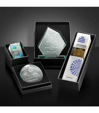Collection of engraved glass awards in black boxes on a dark surface