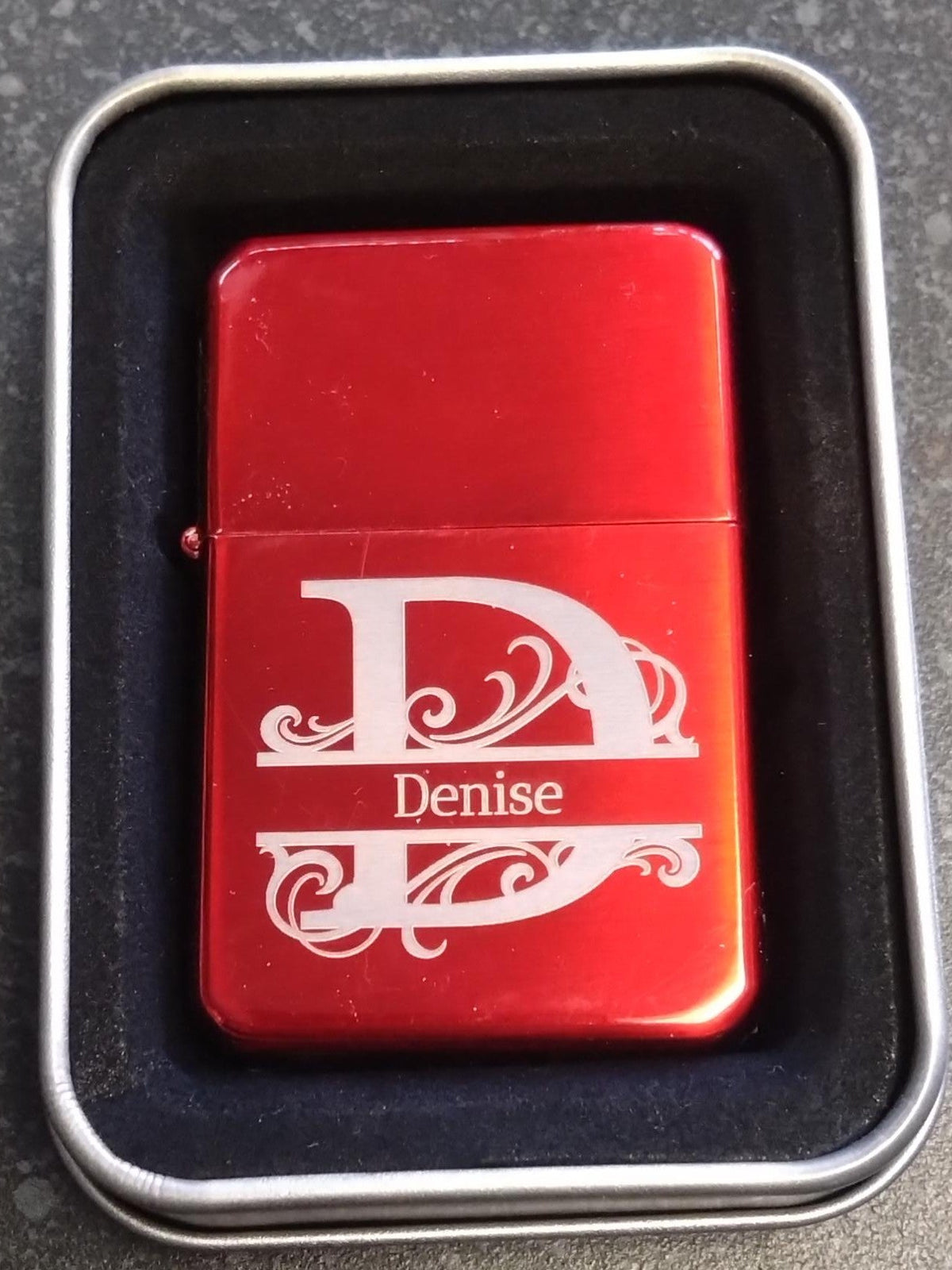 Red lighter with 'Denise' engraving in a metallic case on a dark surface